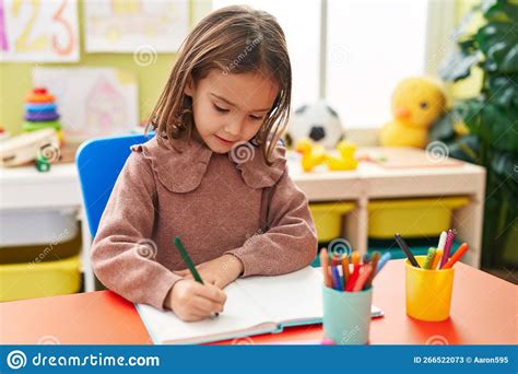 Adorable Hispanic Girl Preschool Student Sitting On Table Writing On