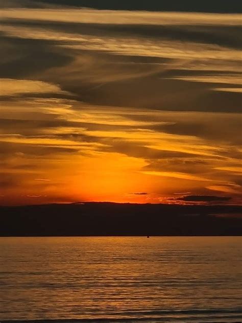 The Sun Is Setting Over The Ocean With Clouds In The Sky