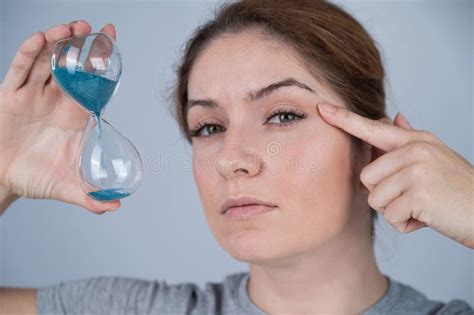 Caucasian Red Haired Woman Holds An Hourglass And Examines The Wrinkles Around Her Eyes Aging