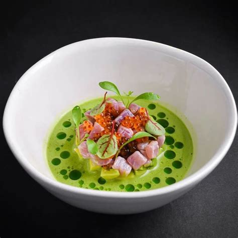 A White Bowl Filled With Green Food On Top Of A Black Countertop Next