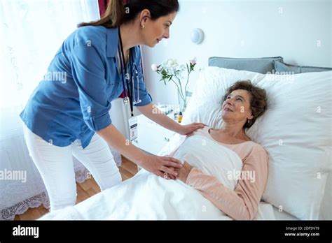 Nurse Leaning Over Elderly Woman Lying In Hospital Bed Senior Female