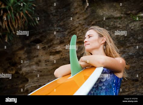 Sportliche Mädchen im Bikini mit Surfbrett stand von schwarzen Felsen