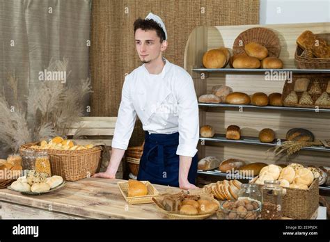 A tall and handsome baker in a baker's outfit stands behind the counter ...