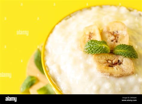 Bowl With Delicious Rice Pudding Banana Slices And Mint Leaves On Yellow Background Closeup