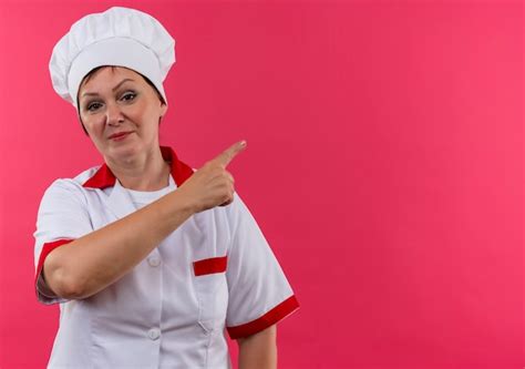 Complacida cocinera de mediana edad en uniforme de chef señala con el