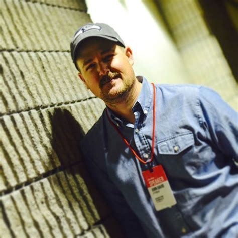 A Man Leaning Against A Brick Wall Wearing A Hat And Tag On His