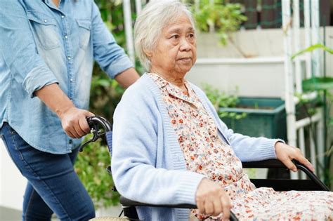 Cuidador ayuda a una anciana asiática con discapacidad sentada en silla