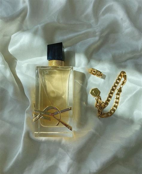 A Bottle Of Perfume Sitting On Top Of A Bed Next To A Chain