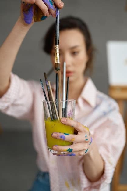 Artista feminina lavando equipamento de pincel em copo de água Foco