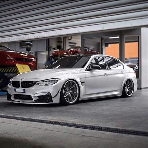 A White Bmw Car Parked In A Garage Next To Two Other Red And Yellow Cars