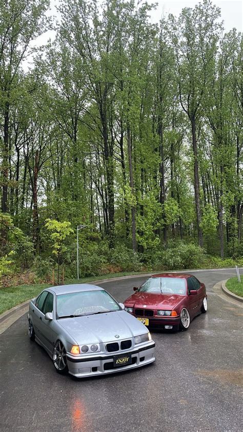 Two Cars Parked On The Side Of A Road In Front Of Some Trees And Bushes