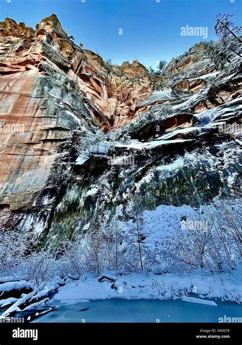 Towering Snow Frosted Icicle Fringed Red Rock Cliff Face Water Stained Blue Ice Blue Sky