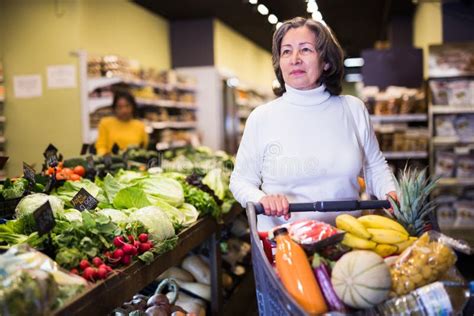 Elderly Woman Walking With Shopping Trolley In Grocery Shop Stock Image