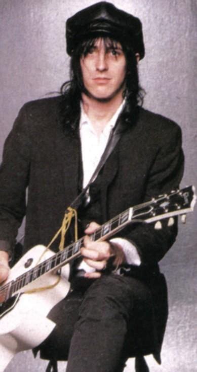 A Man With Long Hair Is Sitting And Playing An Electric Guitar While