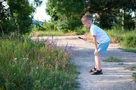 Le Enfant Examine Bleu Fleurs Par Une Grossissant Verre Commun