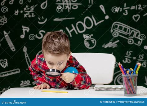 Cute Clever Boy Is Sitting At A Desk With Magnifying Glass In Hand