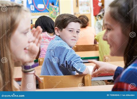 Unhappy Boy Being Gossiped About By School Friends In Classroom Stock