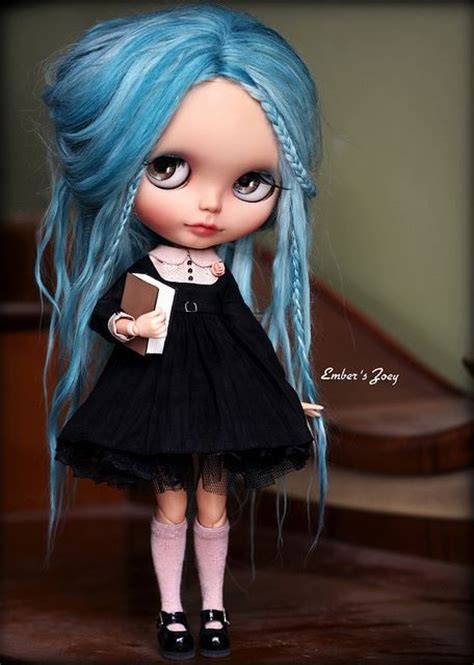 A Doll With Blue Hair Wearing A Black Dress And Holding A Book In Her Hand