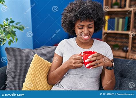 African American Woman Drinking Coffee Sitting On Sofa At Home Stock