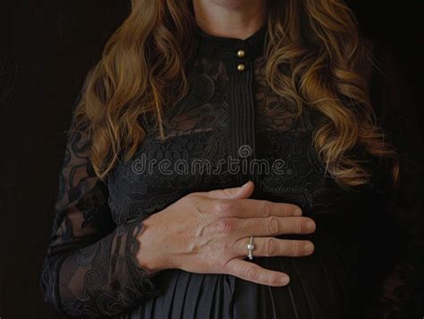 A Pregnant Woman Stands Gracefully In A Black Dress Her Hands