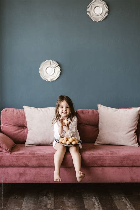 «Little Girl Sitting On Sofa With Food» del colaborador de Stocksy «Alina Hvostikova» - Stocksy