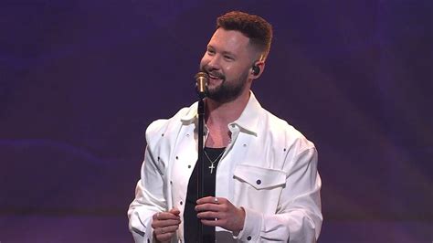 a man in white shirt and tie standing on stage with microphone up to his mouth