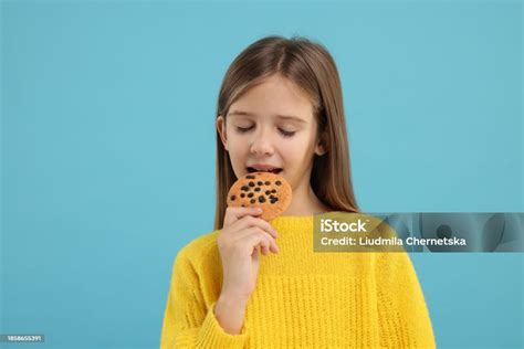 Cute Girl Eating Chocolate Chip Cookie On Light Blue Background Stock