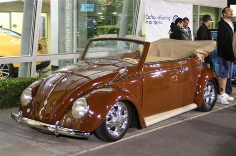 An Old Car Is Parked On The Side Of The Road With People Looking At It