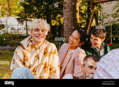 Gay Friends Laughing While Sitting Next To Each Other During Dinner Party In Back Yard Stock