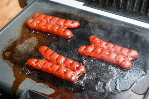 Premium Photo | Three small bratwurst hot dog frankfurter sausages grilled on electric grill.