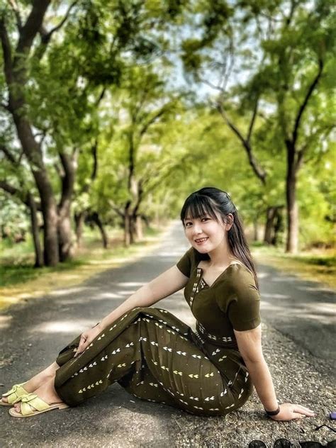 A Woman Sitting On The Side Of A Road In Front Of Some Trees And Shoes