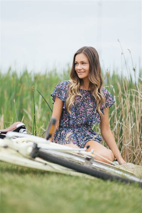 A Young Girl Sitting In A Field Of Tall Grass With Her Bike By