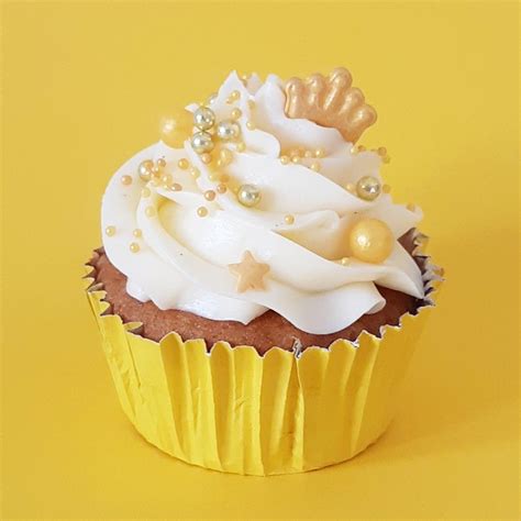 A Cupcake With White Frosting And Gold Decorations