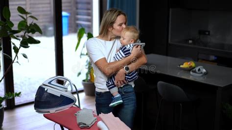 Confident Beautiful Happy Mother Ironing Laundry Talking With Infant