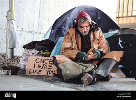 A Homeless Beggar Man With A Carboard Sign Sitting Outdoors In City