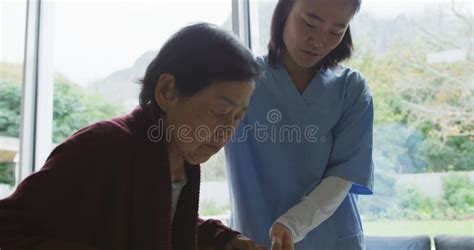 Smiling Asian Female Doctor Helping Senior Female Patient To Walk Using