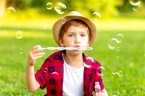 Premium Photo A Little Redhaired Boy Inflates Soap Bubbles On A Green