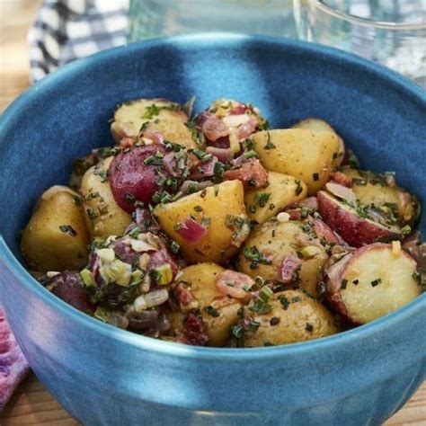 A Blue Bowl Filled With Potatoes On Top Of A Wooden Table Next To Water