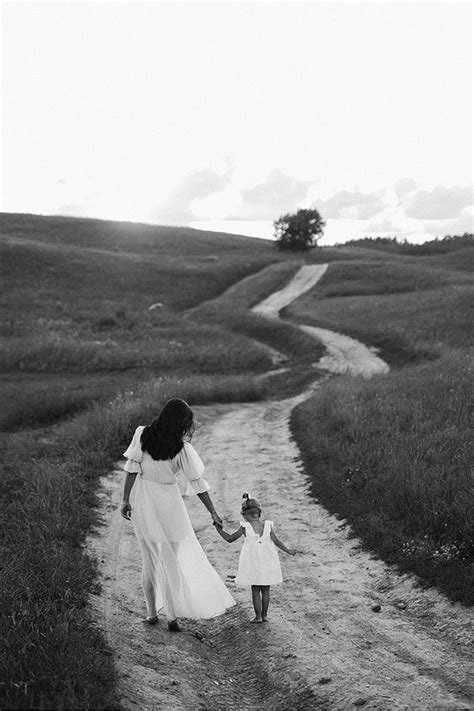 A Mother And Her Daughter Walking Down A Dirt Road Holding Hands In The