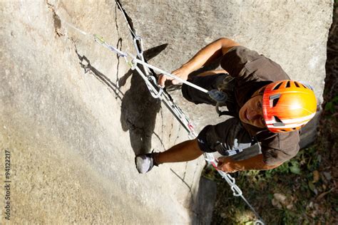 A man wearing a helmet and harness is climbing a rock face on a ...