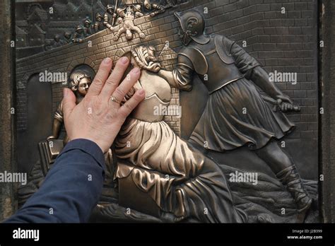 Tourist Touches The Figure Of Saint John Of Nepomuk On The Bronze Plaque On The Charles Bridge