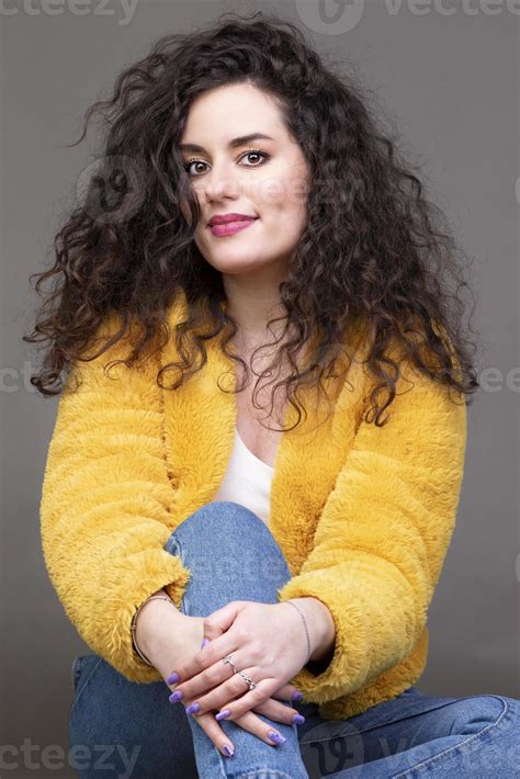 A Beautiful Brunette Girl With Curly Hair In A Yellow Fur Coat Looks At The Camera And Smiles A