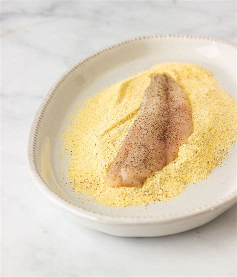 A White Bowl Filled With Yellow Powder And A Piece Of Fish