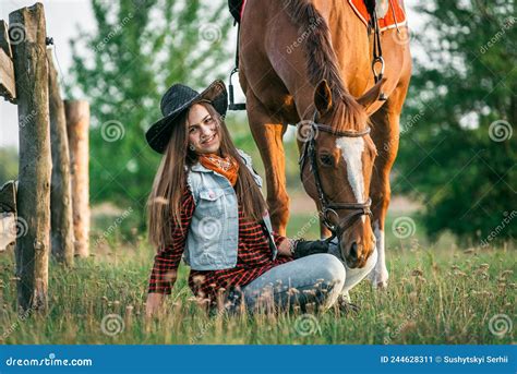 A Cowgirl Sits On The Ground Near Her Horse In A Field In Summer Stock