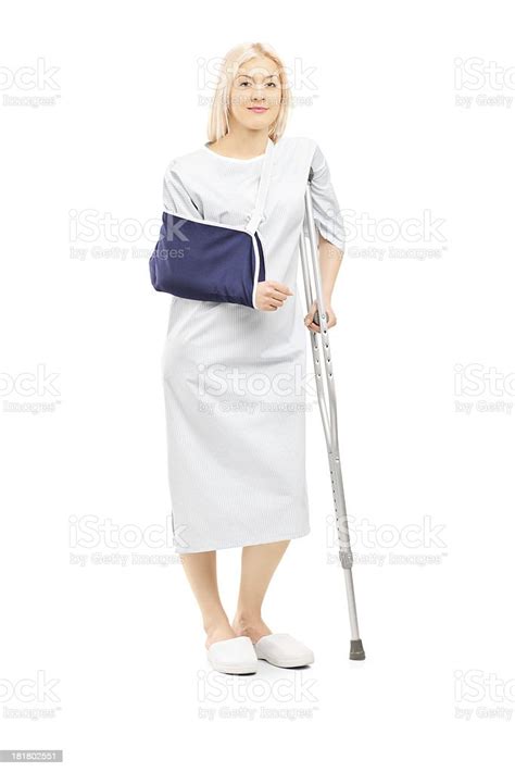 Blond Female Patient In Gown With Broken Arm And Crutch Stock Photo