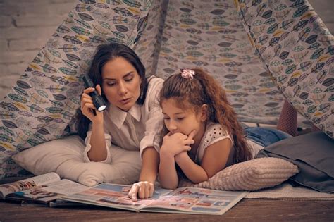 Mãe e filha estão sentadas em uma tenda lendo histórias a lanterna