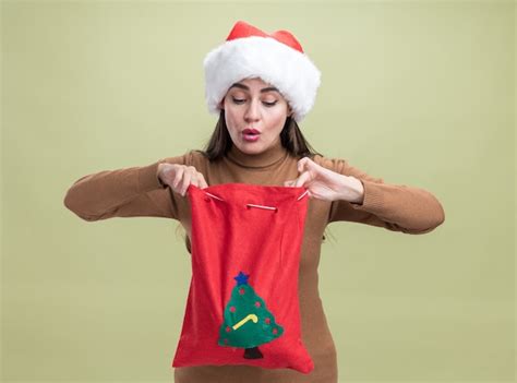 Impresionada joven hermosa niña con sombrero de navidad sosteniendo y