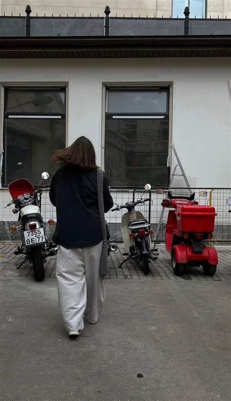 A Woman Walking Down The Street In Front Of Some Parked Scooters And Mopeds