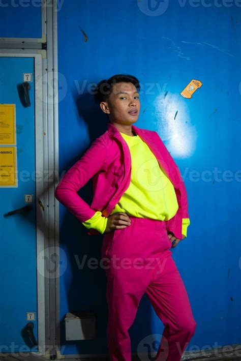 A Gay Asian Man Posing Very Funny And Humorous While Wearing A Pink Suit In Front Of A Blue