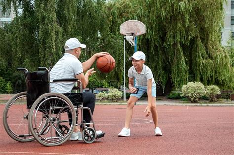 A Man In A Wheelchair Plays Basketball With His Son On The Sports